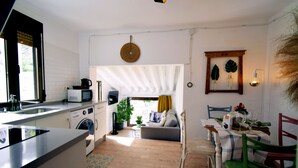 A compact kitchen with a washing machine, a microwave, and a sink. There is a dining area with a table and chairs, and a sofa in the background. - El Orgullo rural house, with terrace and impressive views of the Bailón Canyon. (Zuheros)
