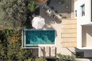 An aerial view of a modern house with a swimming pool, lounge chairs, and a covered patio area. - Massari Hills Luxury Living - Villa Grand Large (Μάσαρη)
