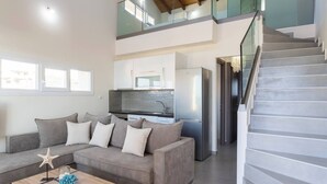 A modern living room with a grey sofa, a wooden coffee table, and a kitchen area with white cabinets and a stainless steel refrigerator.