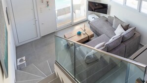 A modern interior with a wooden ceiling, a glass railing, a grey sofa, and a door leading to an outdoor area.