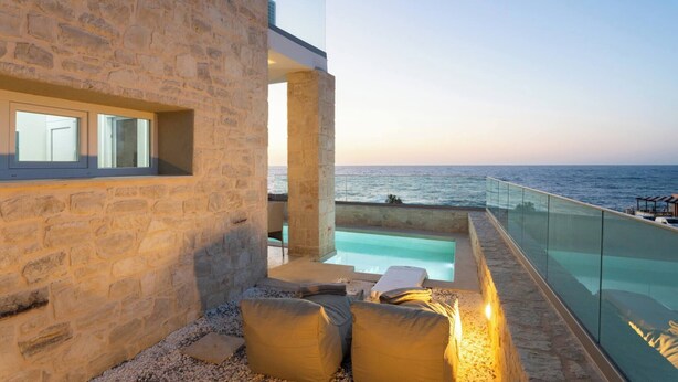 A stone building with a glass infinity pool and outdoor seating.