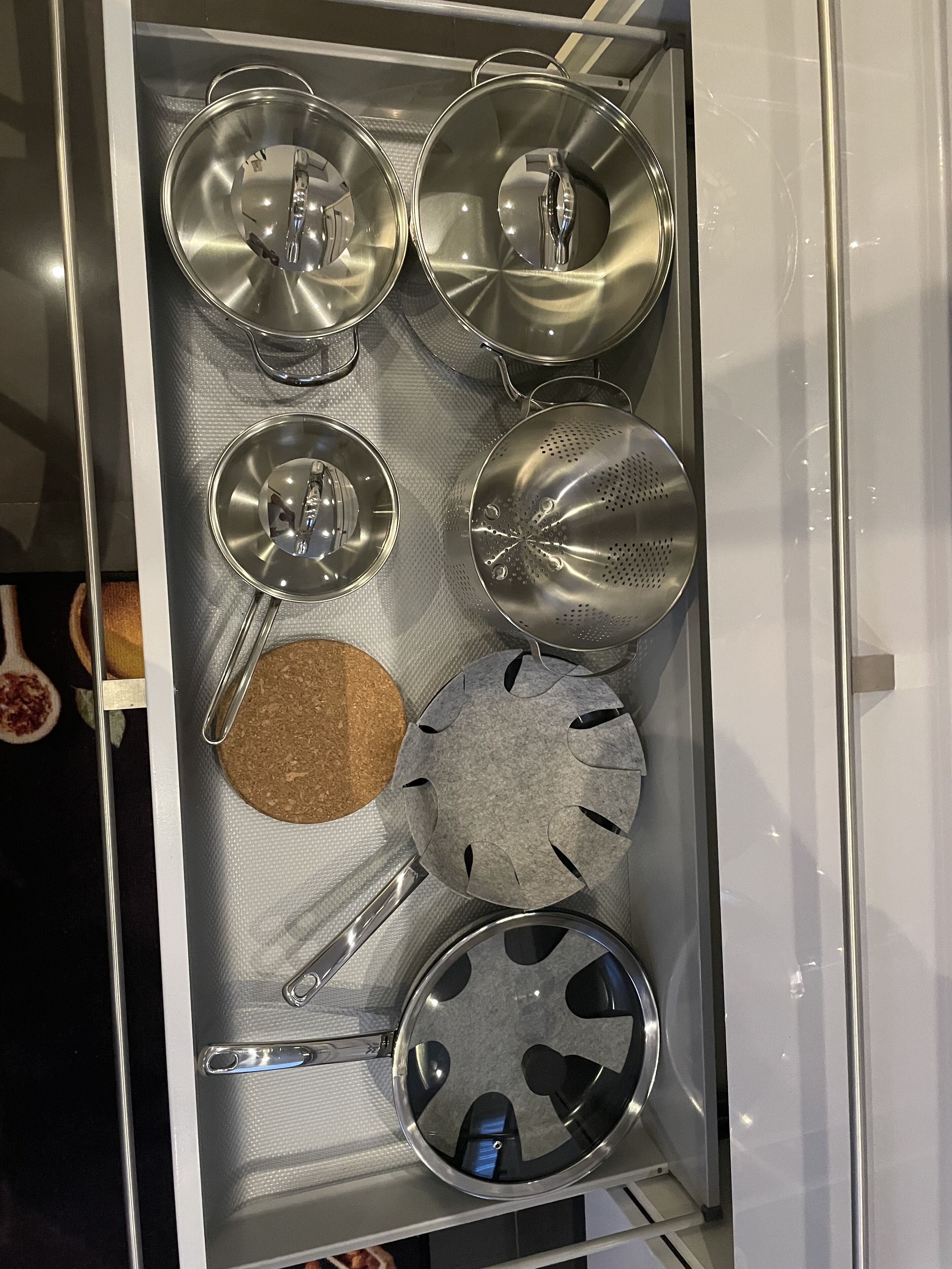 Un cajón de cocina con diversos utensilios y utensilios de cocina de acero inoxidable, incluyendo ollas, sartenes y un colador.