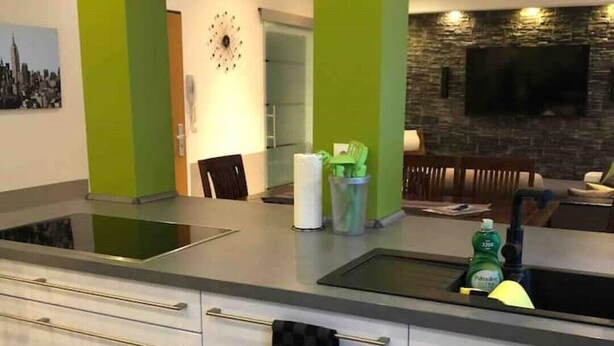 A modern kitchen with a central island, green accent walls, a built-in oven, and a flat-screen TV mounted on a stone wall. - TOP APARTMENT- 2 floors - 100 m² - up to 10 people (Dortmund)