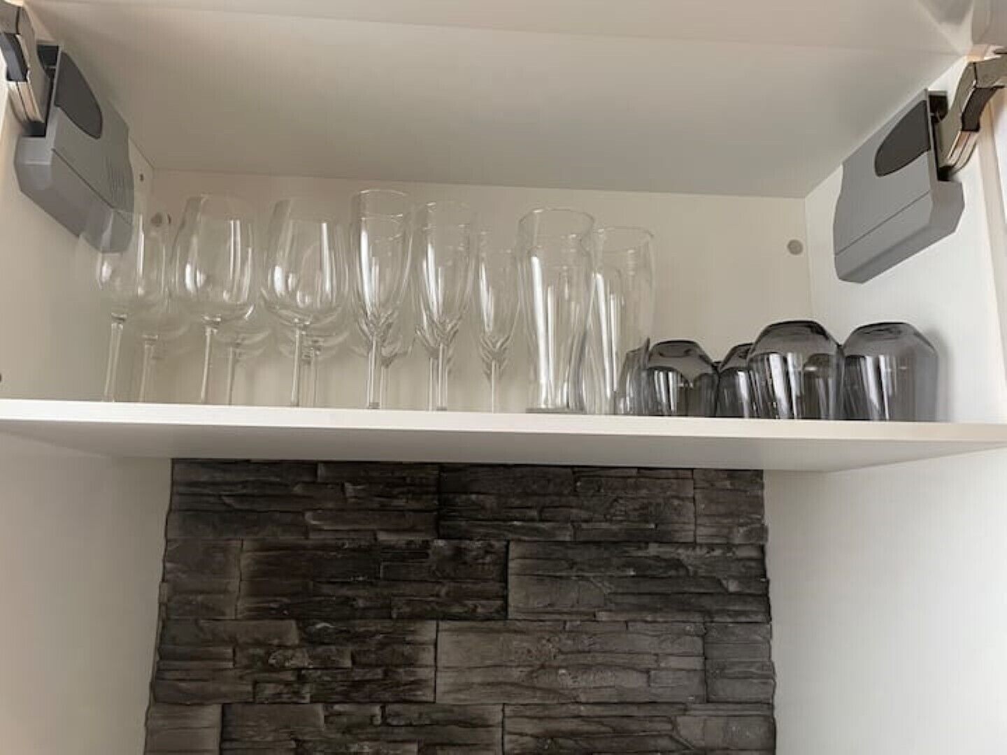 A kitchen shelf with wine glasses and stainless steel containers.