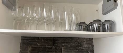 A kitchen shelf with wine glasses and stainless steel containers.