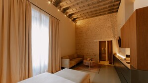 A modern hotel room with a large bed, a sofa, a small round table, and a kitchen area with wooden cabinets. - Casa del Cardenal (Córdoba)