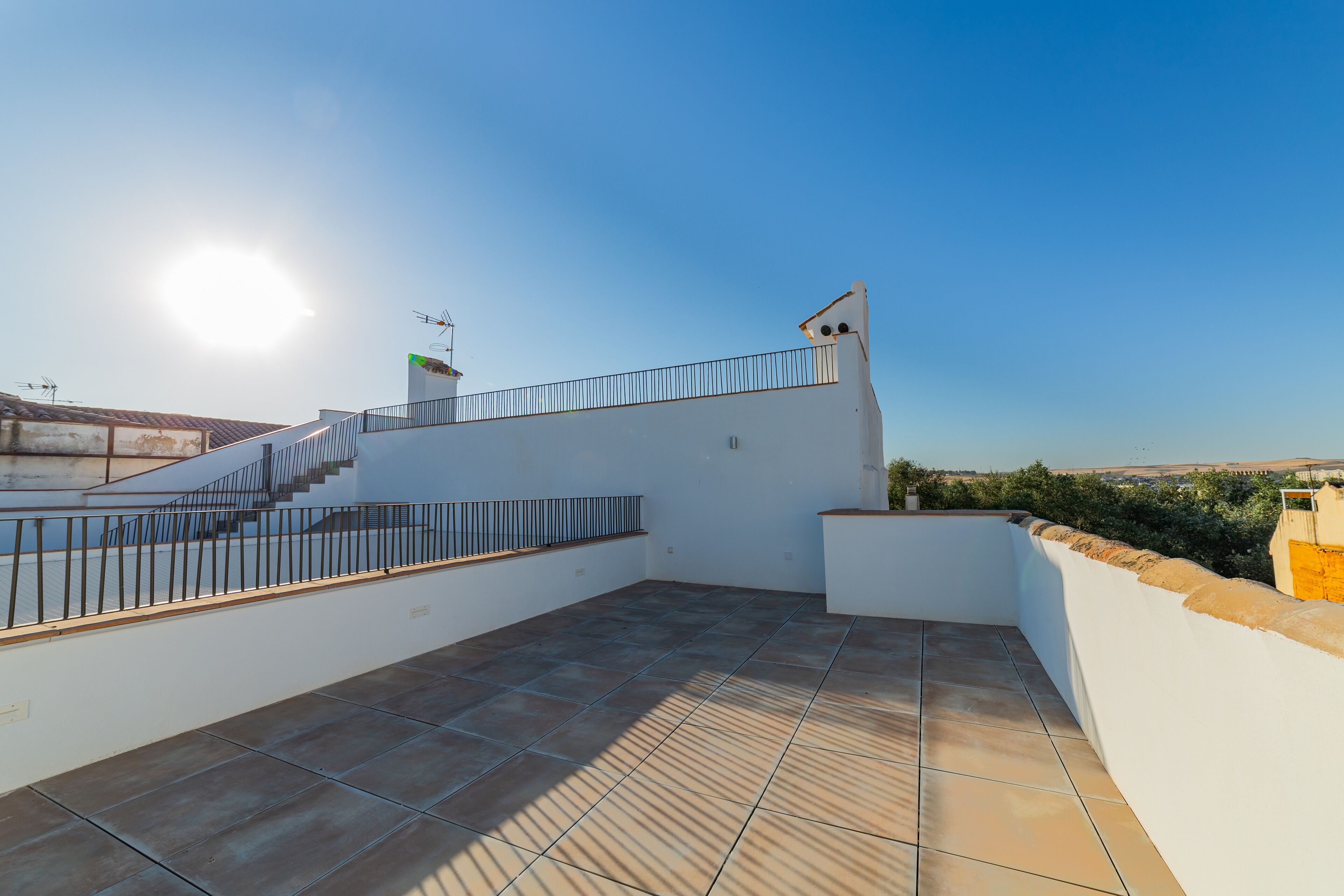 A rooftop terrace with a tiled floor, a metal railing, and a clear view of the landscape.