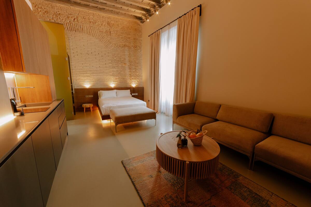 A modern hotel room with a bed, sofa, and a small dining area.