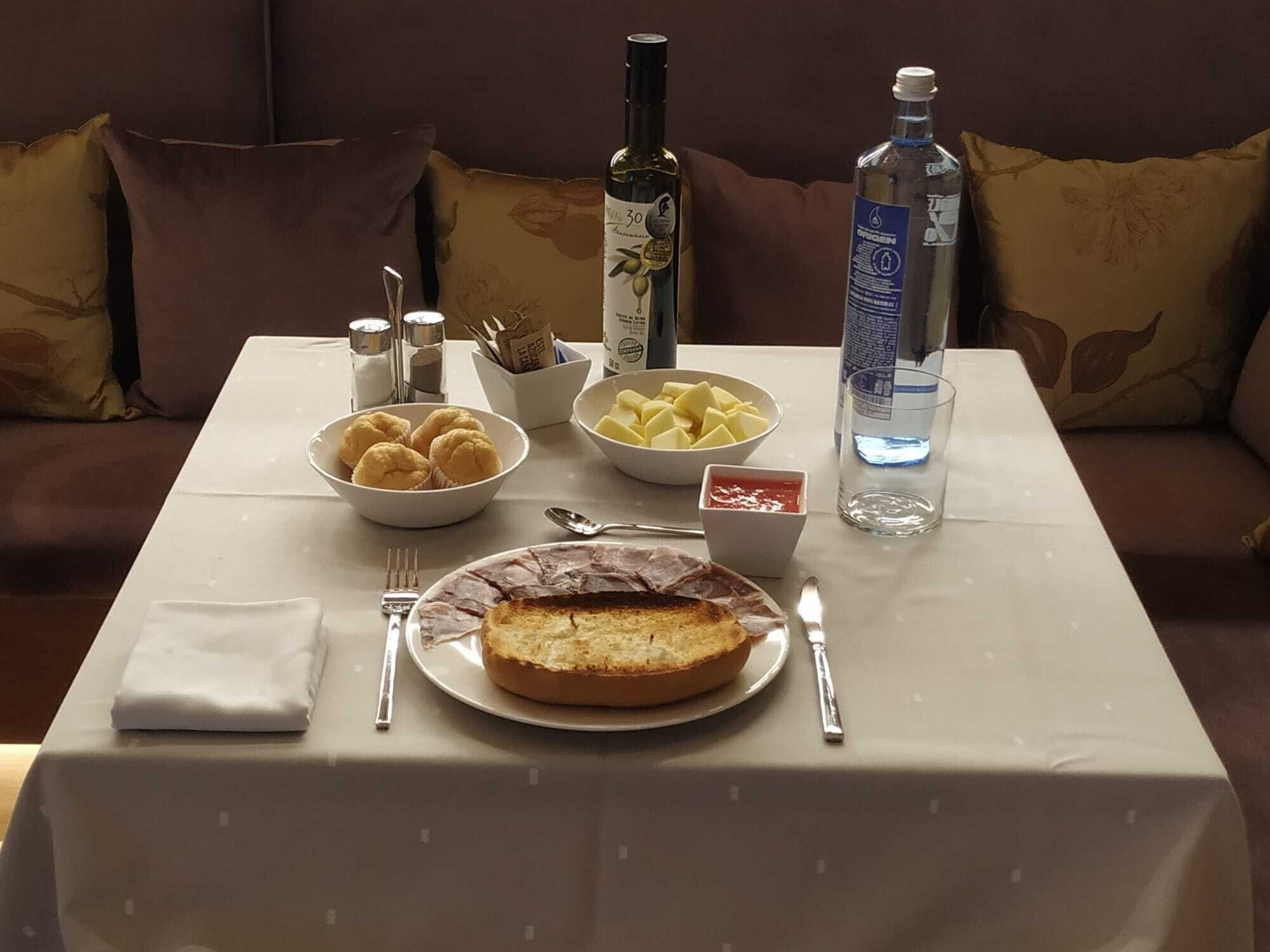 A dining table with a plate of bread, a bowl of cookies, a bottle of water, and condiments.