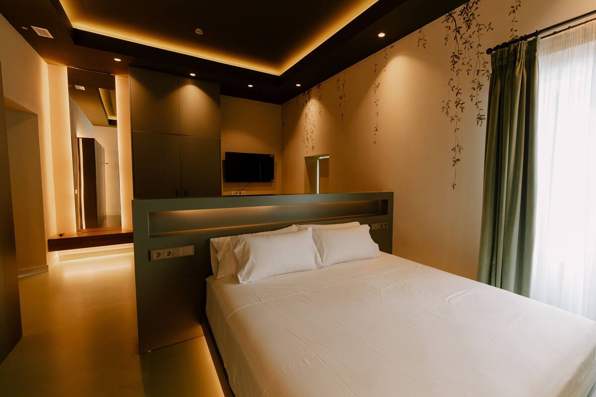 A modern hotel room with a large bed, a flat-screen TV, and a bathroom with a mirror and sink.