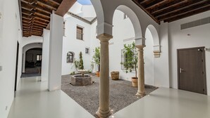 A spacious courtyard with white walls, wooden beams, and columns. There are potted plants and a fountain. - Casa del Cardenal (Córdoba)