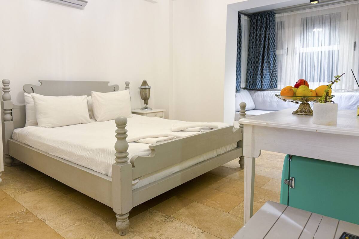 A neatly arranged bedroom with a bed, bedside table, lamp, and a fruit bowl on a dresser.