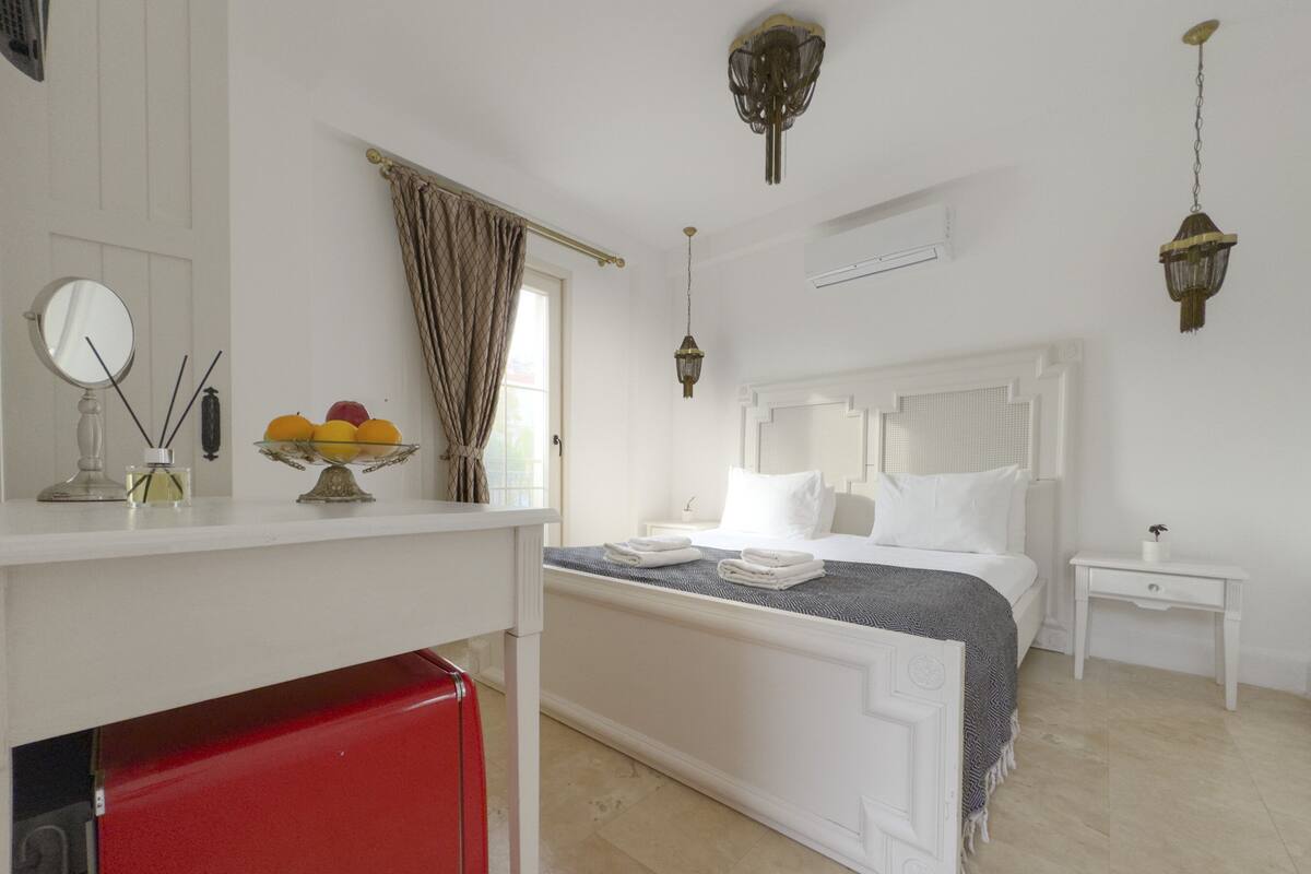A hotel room with a bed, bedside tables, a red refrigerator, a window with curtains, and a ceiling fan.