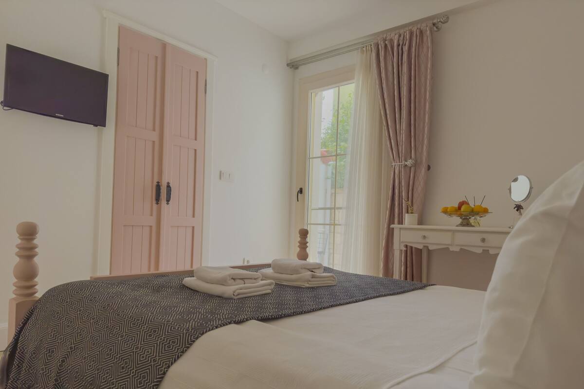 A bedroom with a bed, a dresser, a TV, and a window with curtains.