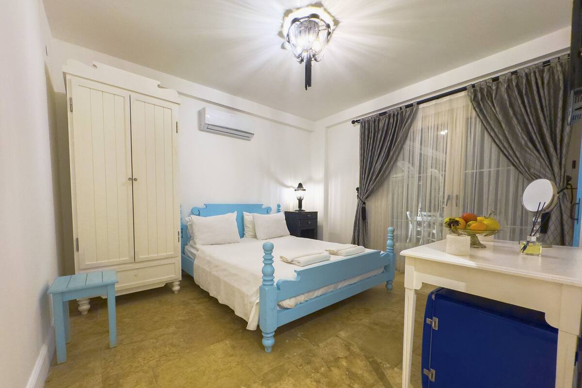 A bedroom with a bed, a desk, a wardrobe, and a window with curtains.