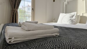 A neatly made bed with folded towels, a patterned rug, and a hanging lamp. - Fedora Alacati (Cesme)