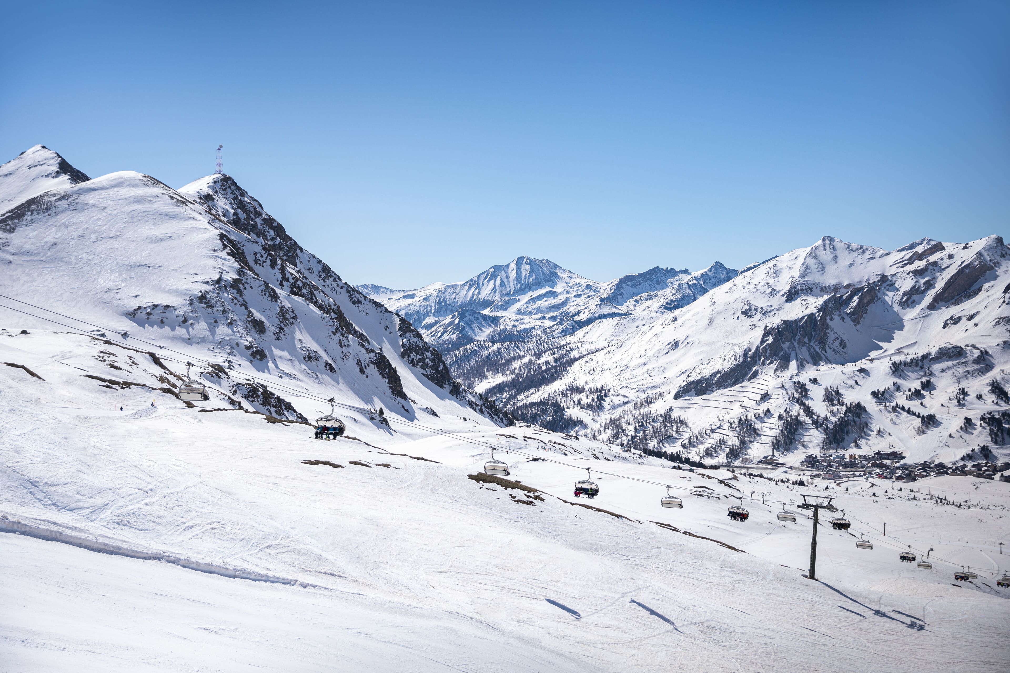 Ein schneebedeckter Berghang mit Seilbahnen und blauem Himmel.