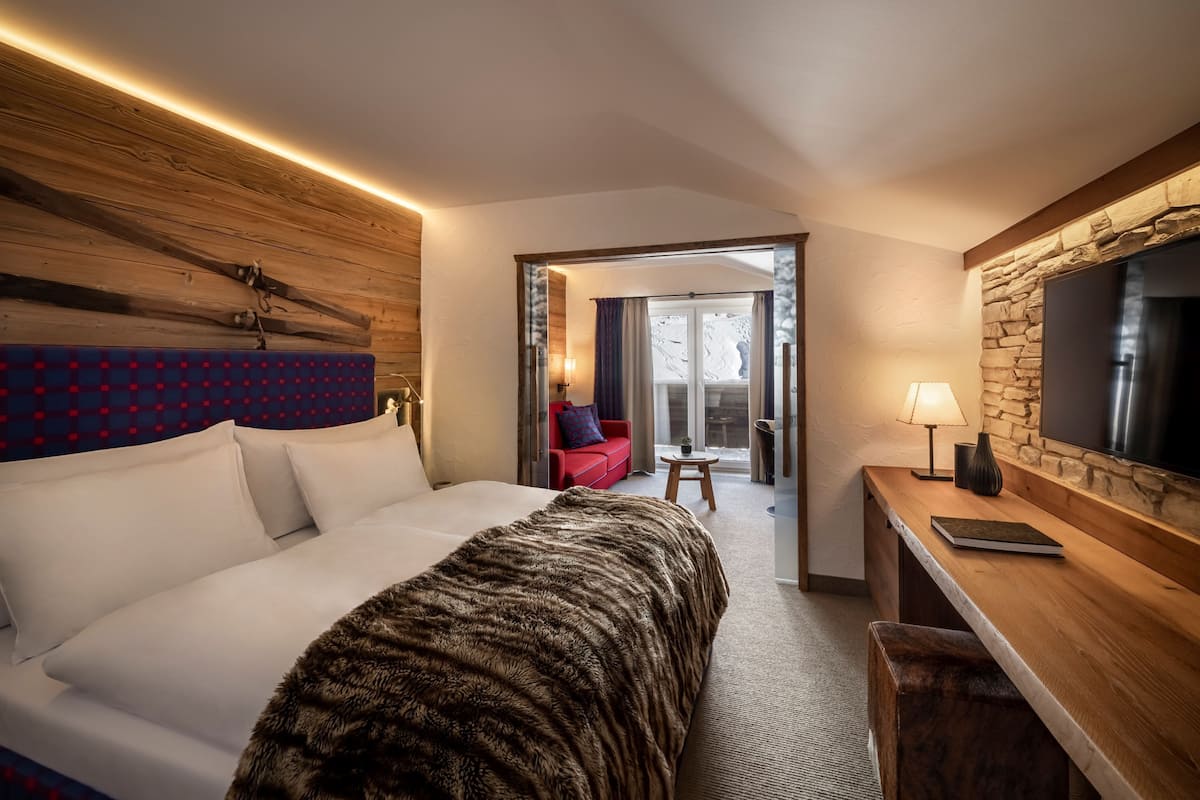 A modern hotel room with a large bed, a wooden headboard, a desk with a lamp, and a television.