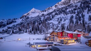 A snow-covered mountain landscape with a hotel featuring multiple floors and a ski lift in the foreground. - Kesselspitze Hotel & Chalet, Valamar Collection (Tweng)