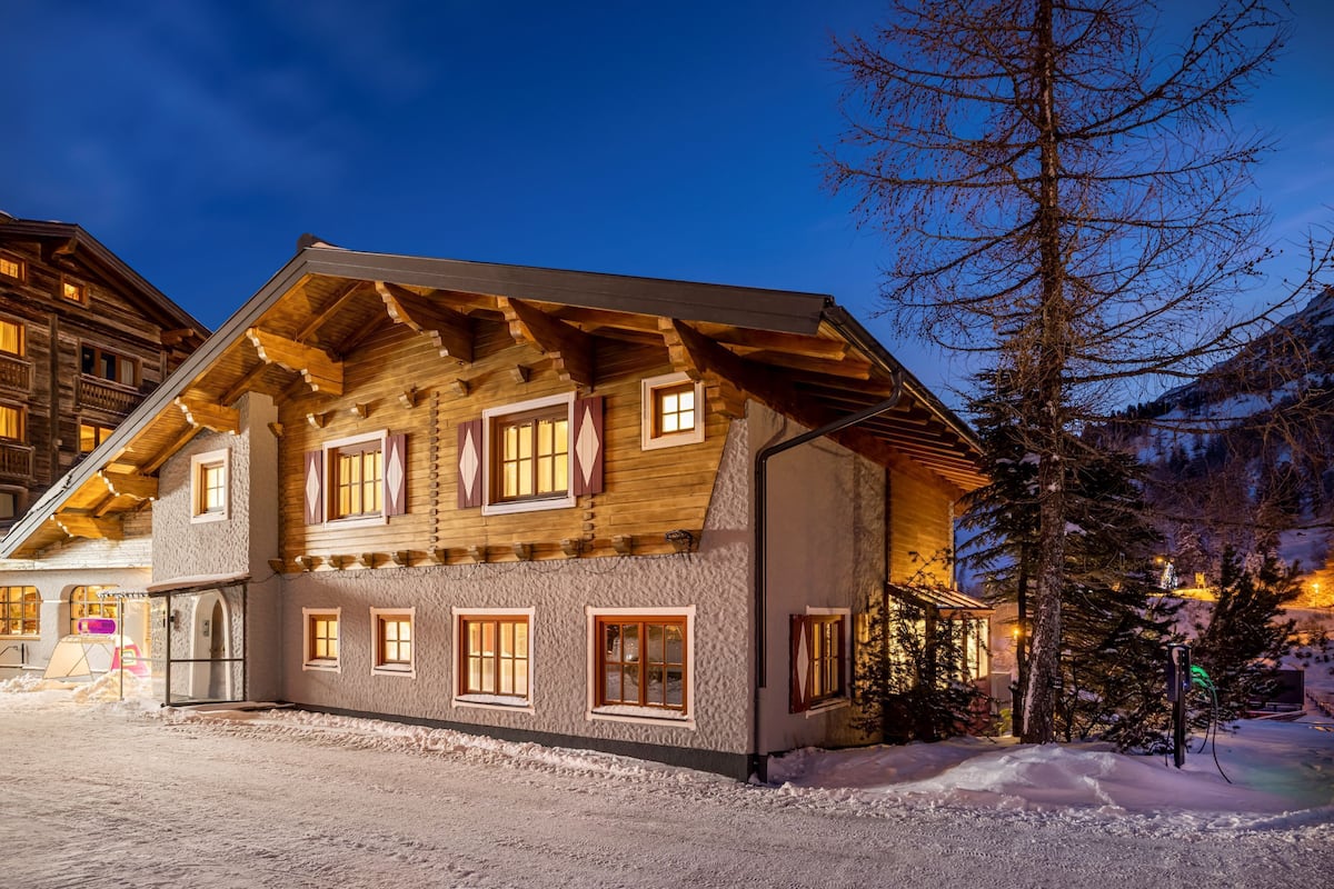 A log cabin-style building with multiple windows and a sloped roof, surrounded by snow and trees.