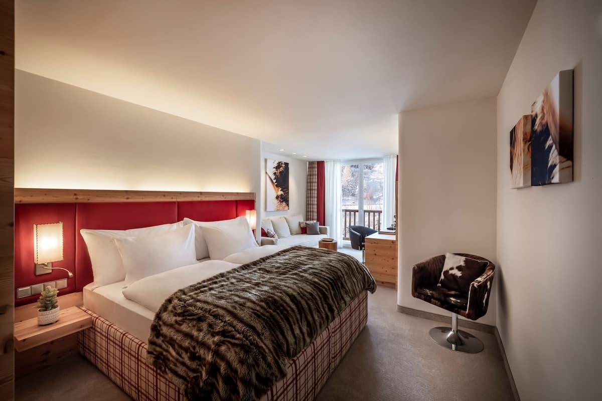 A modern bedroom with a large bed, a red headboard, a small desk, and a chair.