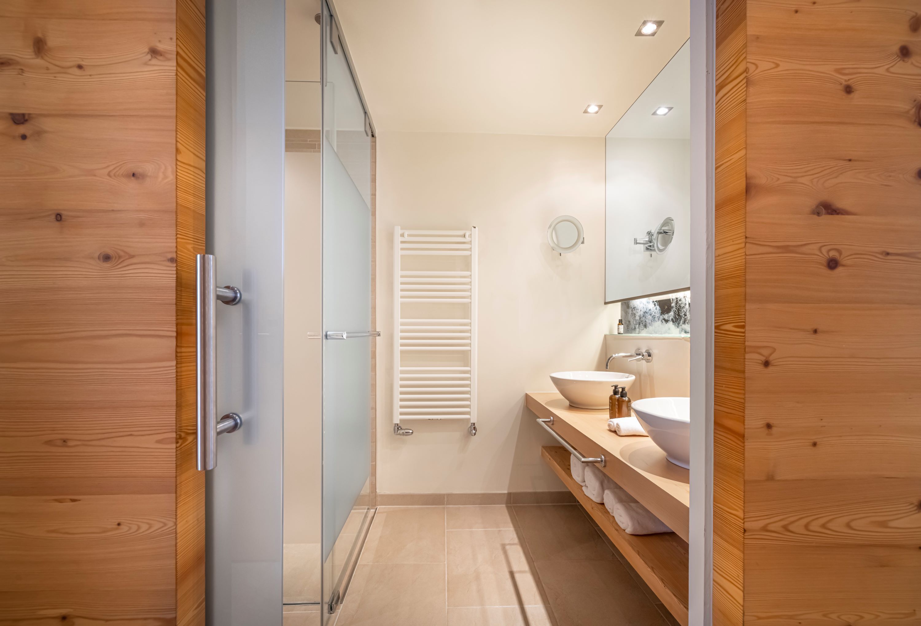 A modern bathroom with a wooden vanity, a large mirror, and a towel rack.