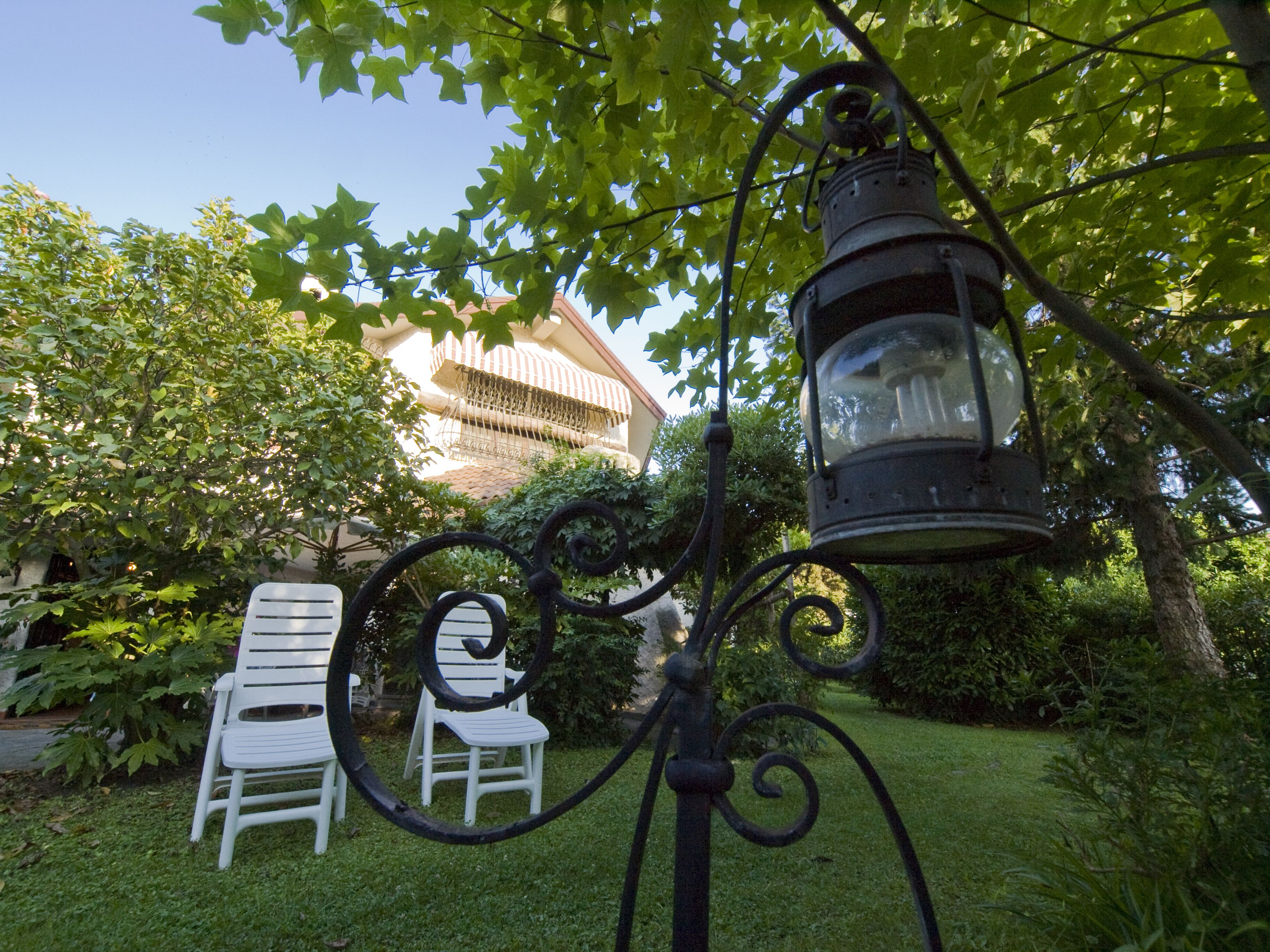 A garden with a metal lamp post, white chairs, and a building with a balcony in the background.