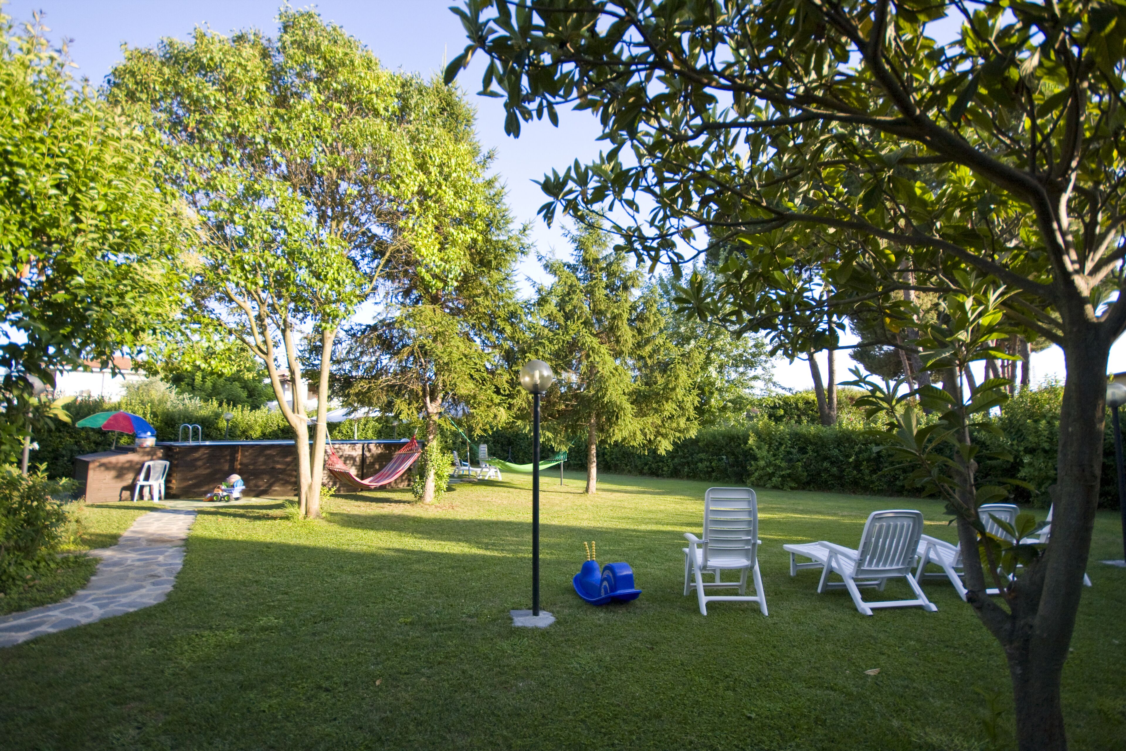 A grassy outdoor area with a hammock, lounge chairs, and a pathway.