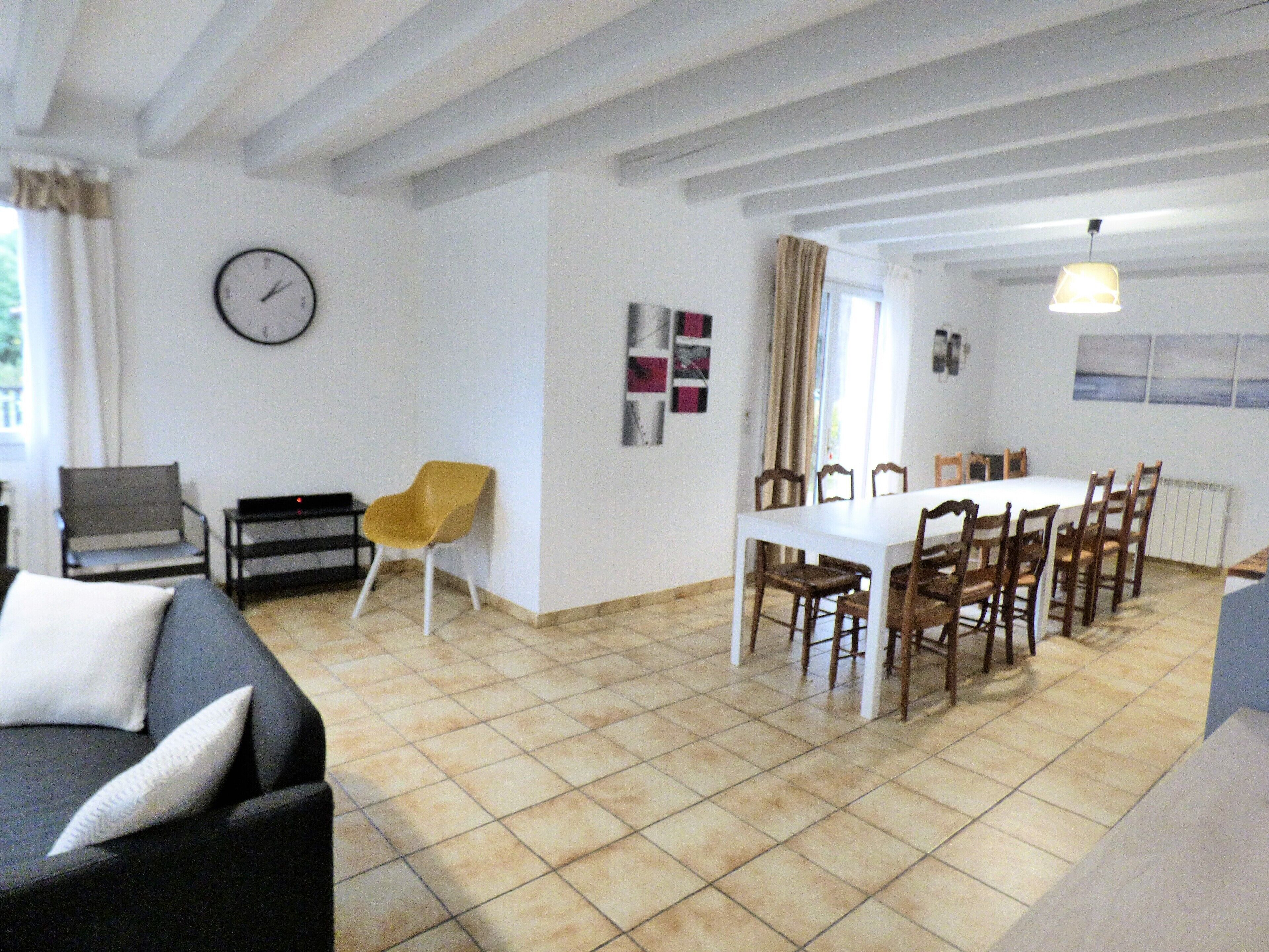 A dining area with a white table and chairs, a clock on the wall, and a sofa with a pillow.
