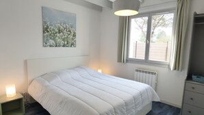 Une chambre à coucher avec un lit, une table de chevet, une fenêtre, un radiateur et un tableau accroché au mur.
