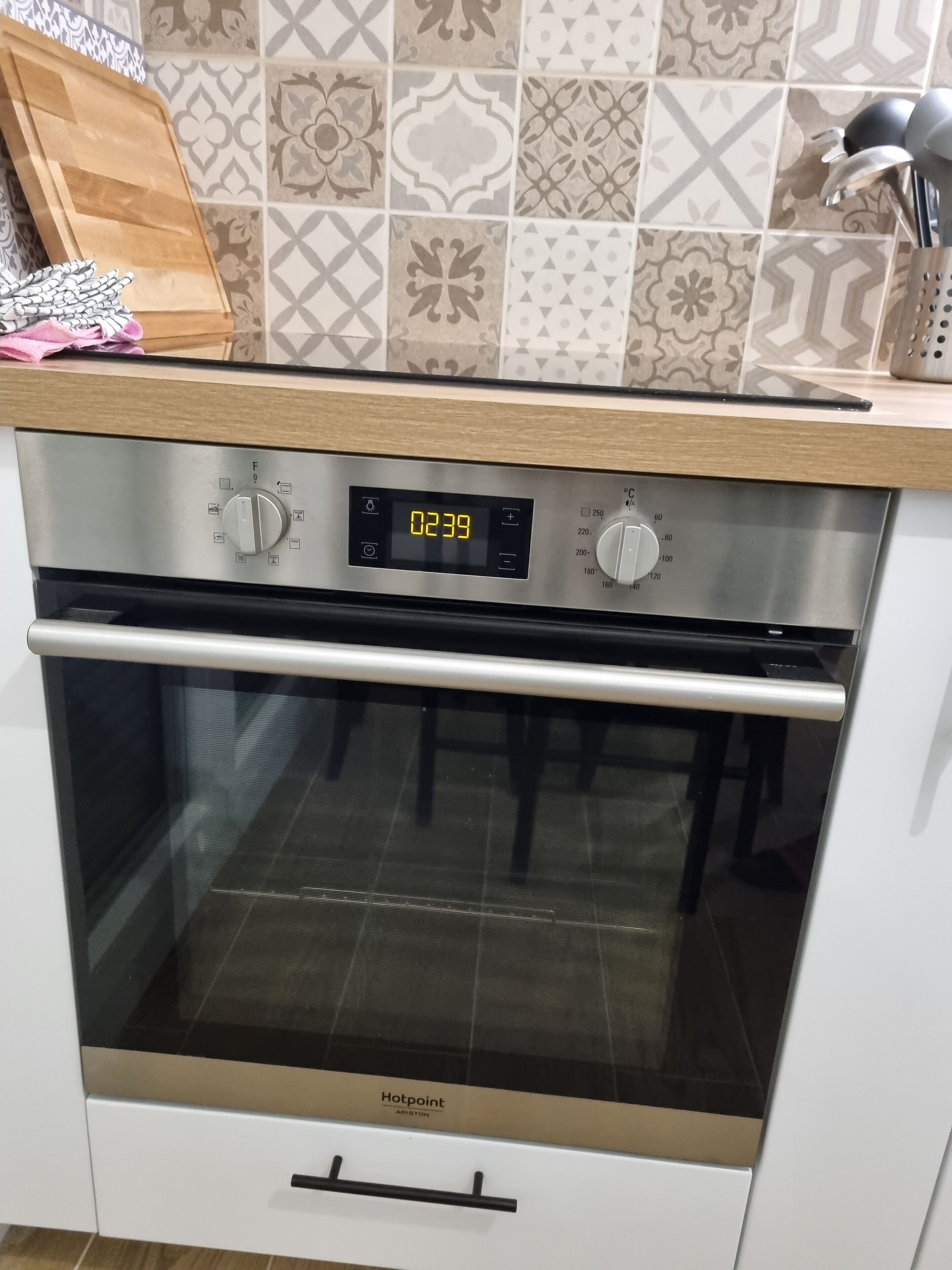 A kitchen with a built-in oven, a digital clock, and a wooden cutting board on the countertop.