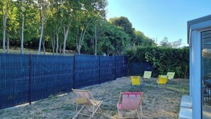 Un jardin avec une clôture bleue, une terrasse en bois et deux chaises de jardin.