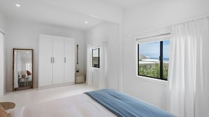 Un dormitorio con cama, armario, espejo, ventana con vistas y una mesita de noche con lámpara.