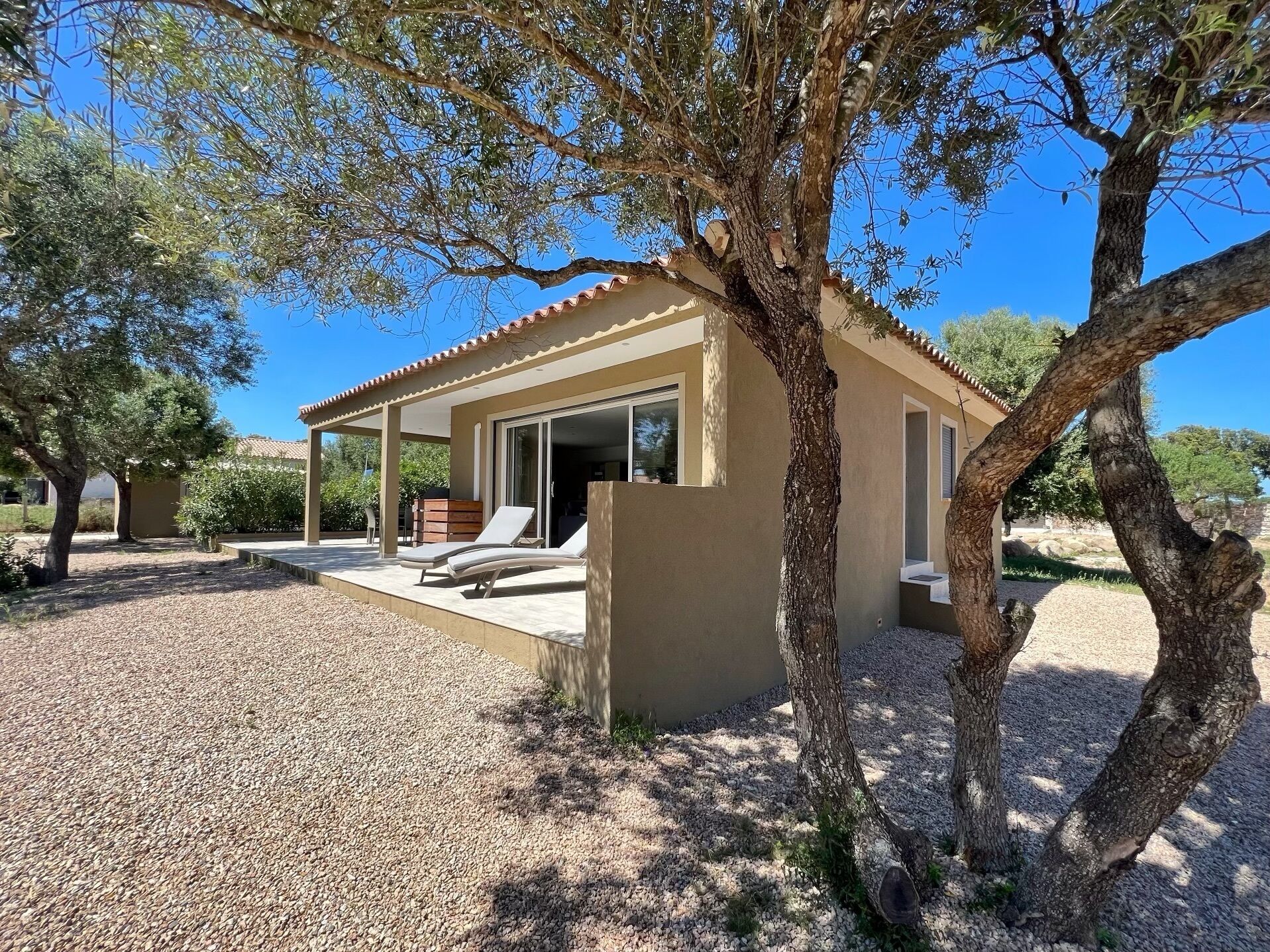 Une maison moderne dotée d’un patio, de deux fauteuils de jardin et d’une allée gravillonnée.