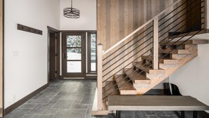 A modern interior with a wooden staircase, a hallway with a door leading outside, and a pendant light.