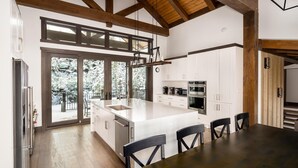 A modern kitchen with white cabinetry, a large island, and a wooden ceiling.