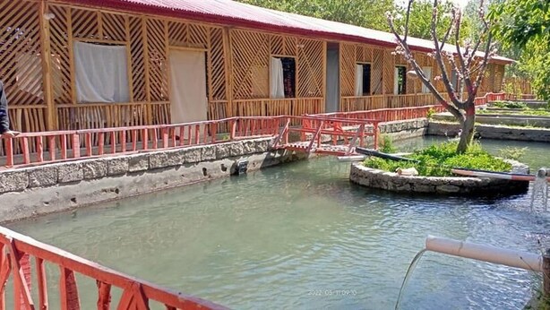 A traditional wooden building with a red roof, a stone pathway, and a small pond with a bridge.