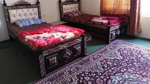 Two double beds with ornate headboards, a patterned rug, and a window with curtains.