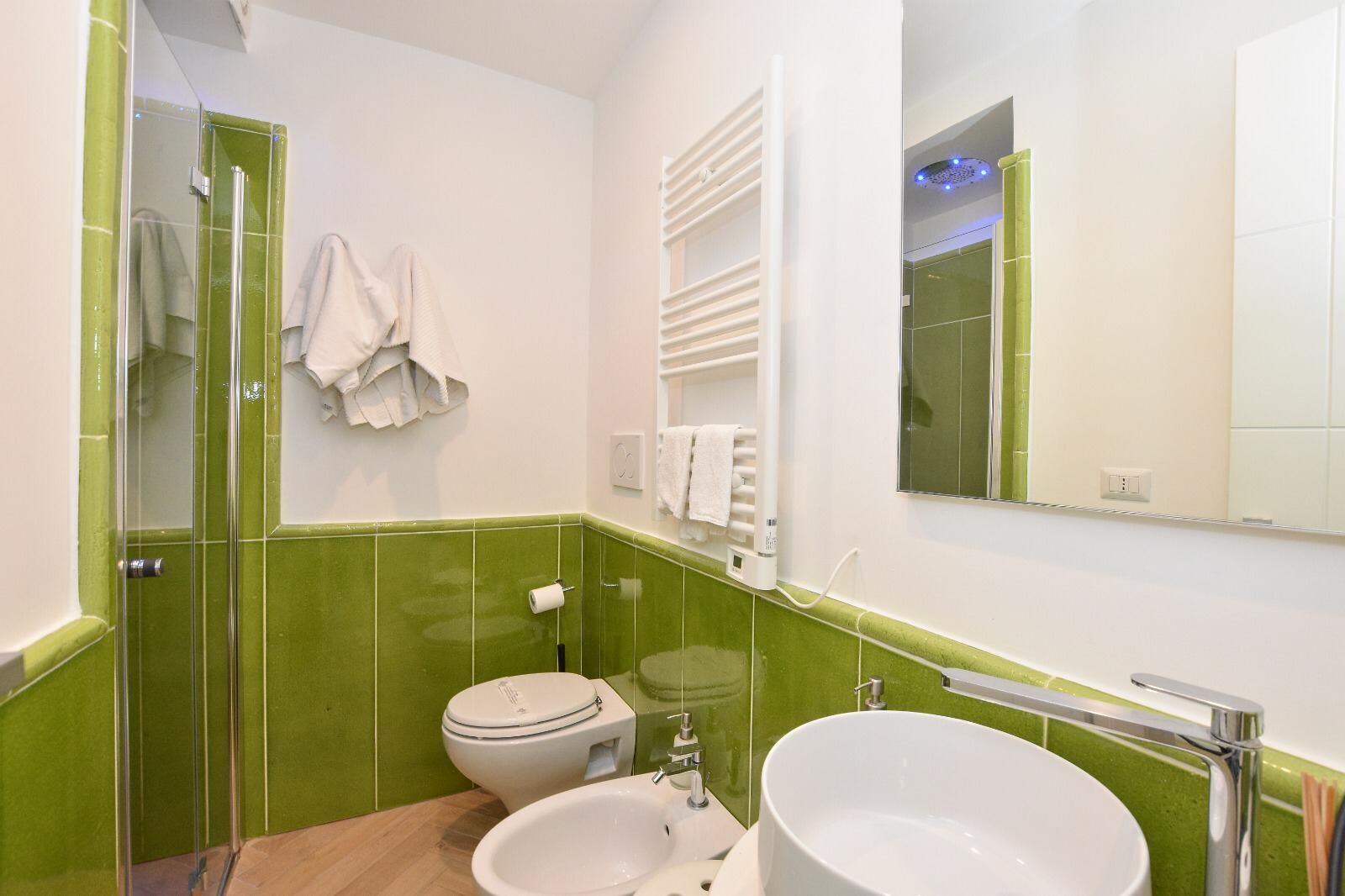 Ein Badezimmer mit grünen Fliesen, einem weißen Waschbecken, einer Toilette und einer Duschkabine aus Glas.