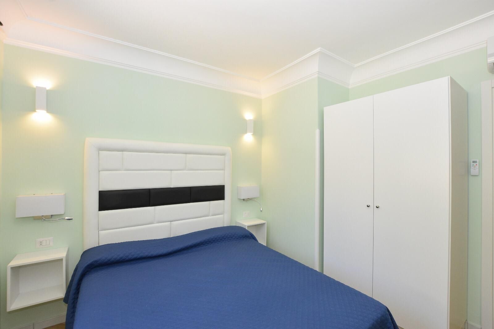 A bedroom with a bed, bedside tables, a wardrobe, and wall-mounted lighting.