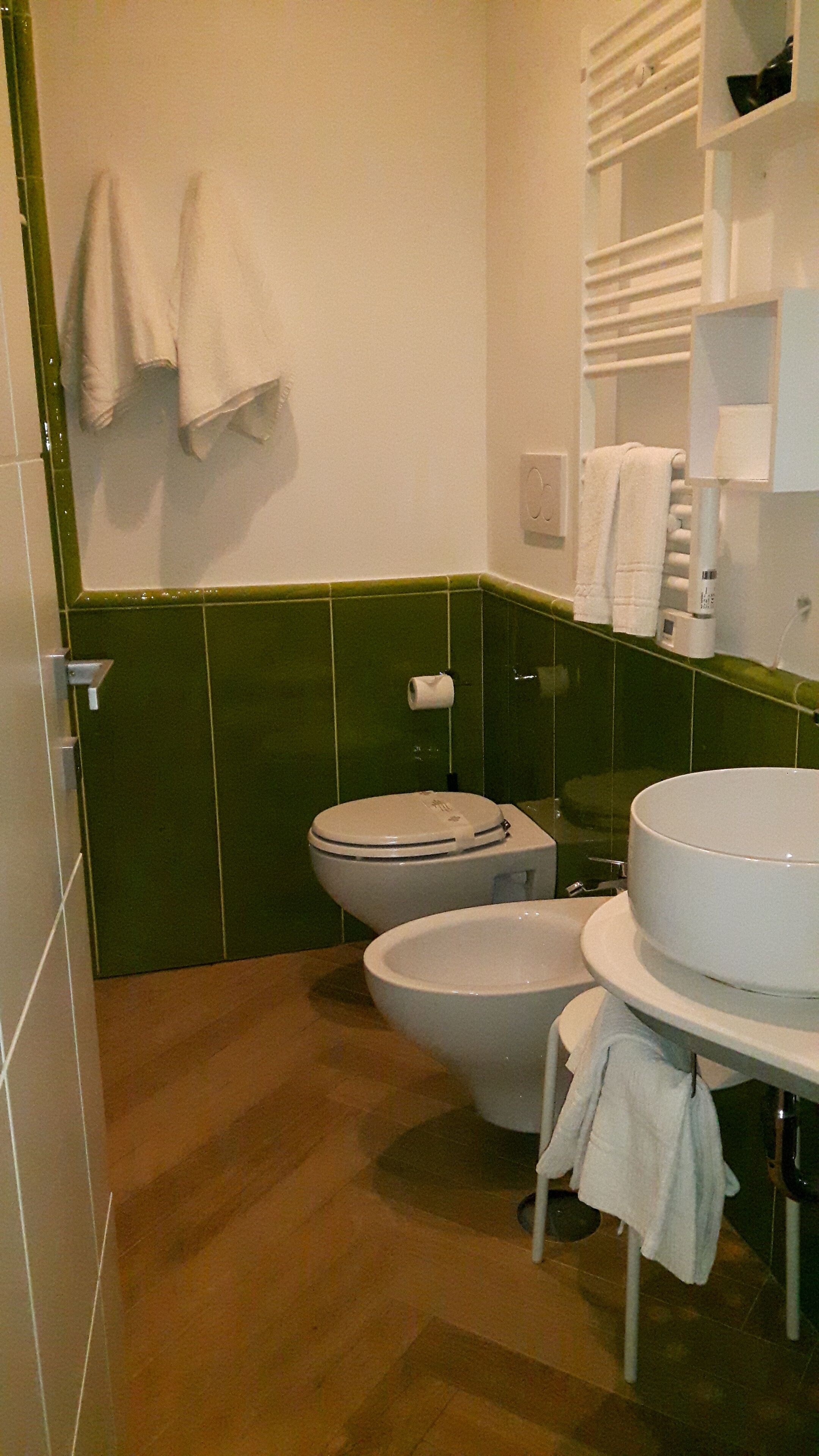 A bathroom with a toilet, bidet, and sink. There are towels hanging on the wall and a toilet paper holder.