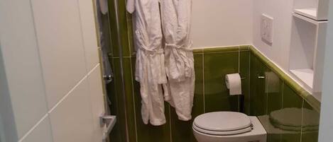 Une salle de bain avec deux toilettes, un lavabo et un miroir. Des serviettes blanches sont suspendues à un porte-serviettes.