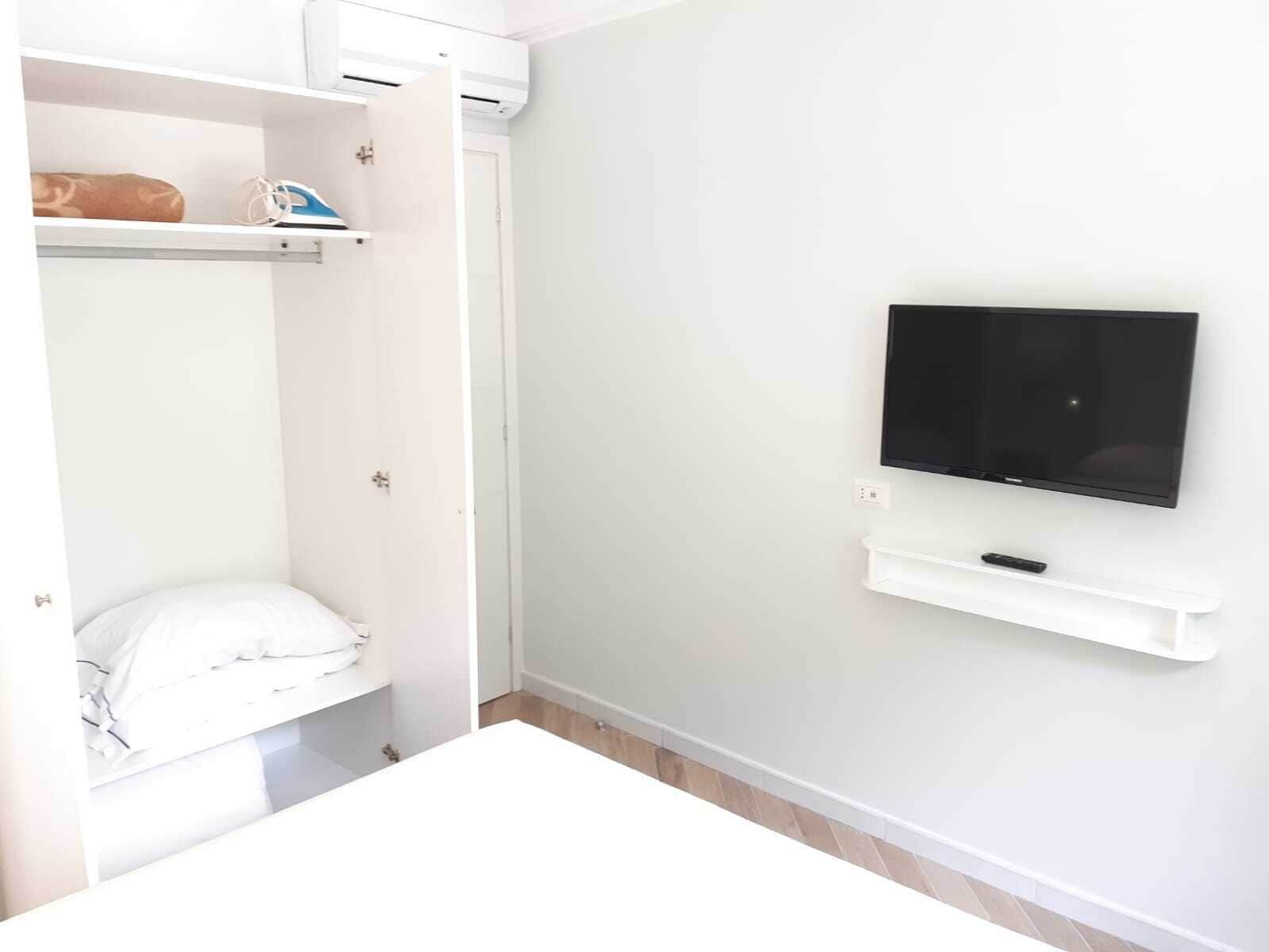 A bedroom with a bed, a TV mounted on the wall, and a white wardrobe.