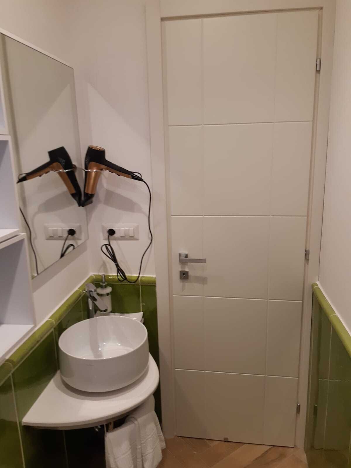 A bathroom with a white sink, a mirror, and two hair dryers mounted on the wall.