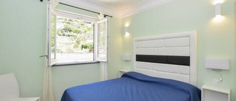 A bedroom with a bed, a window with curtains, a bedside table, and a wall-mounted light.