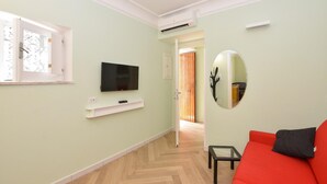 A room with a television on a white shelf, a red sofa, a small table, and a mirror on the wall. - Apartament CARPEDIEM in the Historical center, accessible by 59 steps At 650mt from the Cathedral (Amalfi)
