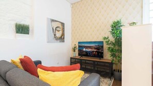 Una sala de estar con sofá, televisión, un cuadro de Buda y una planta en maceta.