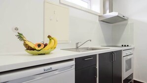 Una cocina moderna con armarios blancos, lavavajillas integrado, horno de acero inoxidable y un frutero sobre la encimera.