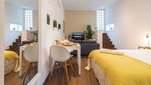 Una habitación de hotel moderna con una cama, un área de comedor con mesa y sillas, un sofá y un televisor.