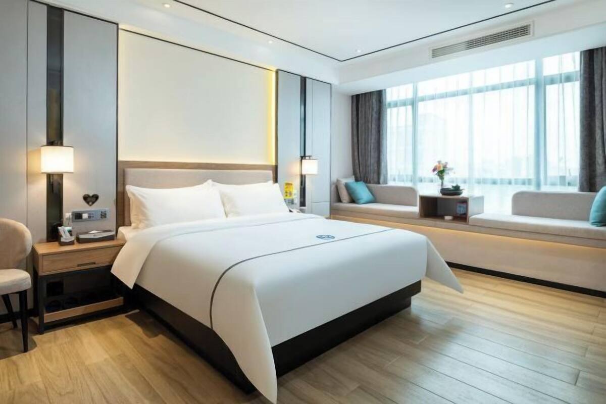 A modern hotel room with a large bed, bedside tables, a sofa, and a window with curtains.